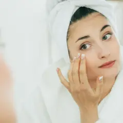 Mujer con toalla en la cabeza aplicándose crema, buscando productos que significan no comedogénico para cuidar su piel.