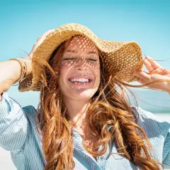 Mujer sonríe con sombrero de paja, aprendiendo como cuidar el pelo en verano.