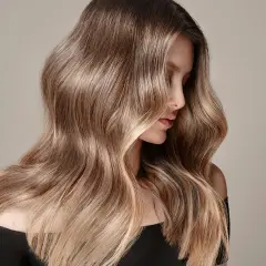 Mujer con cabello largo y ondulado, con un degradado de color que va de oscuro a rubio. Un ejemplo de cómo aclarar el pelo teñido para un look natural.