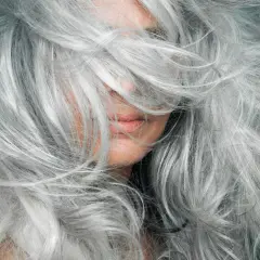 Una mujer con una cascada de cabello plateado, mostrando la belleza de la transición a canas.