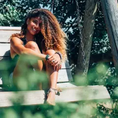 Chica con pelo rizado y voluminoso, sonriendo sentada en un columpio. ¡Así se consigue como rizar el pelo con espuma!