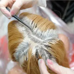 Manos enguantadas aplican tinte en las raíces del cabello rubio. Decolorar el pelo es malo, puede dañar la salud capilar.