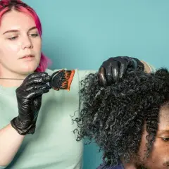 Mujer con pelo rosa aplica tinte a cabello rizado. ¿Cuánto dura un tinte de pelo? Depende del cuidado.