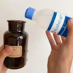 Manos vierten alcohol de romero en un frasco de vidrio ámbar. El alcohol de romero sirve para desinfectar y aliviar dolores.