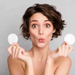 Mujer sorprendida con discos de algodón, mostrando para que sirve el agua micelar para una limpieza facial suave y efectiva.