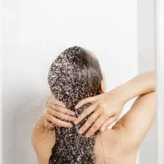 Persona disfrutando de un refrescante lavado de pelo bajo la ducha, con el agua cayendo sobre su cabello oscuro y las manos masajeando suavemente.