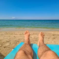 Piernas bronceándose en la playa. El sol de las 7 de la tarde pone moreno mientras disfrutas del mar azul y la arena dorada.