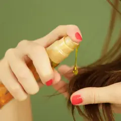 Manos aplicando aceite de ricino para el pelo, una gota dorada cae sobre las puntas.