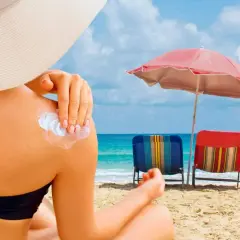 Persona aplica protector solar en su hombro para protegerse de los rayos UVB en un día soleado en la playa.