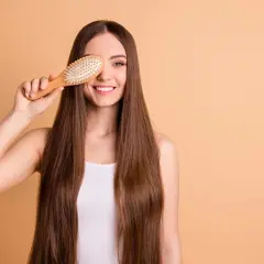 Mujer sonriente con pelo largo y liso, usando un cepillo de madera para mostrar cómo desenredar un pelo muy enredado.