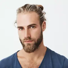Chico con barba y mechas rubias recogidas en un moño. Su mirada es intensa y directa.