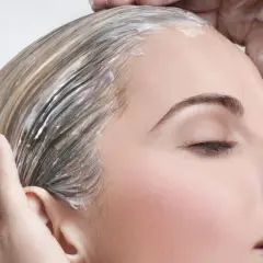 Manos aplican mascarilla en pelo seco antes de lavar, nutriendo cada hebra para un cabello suave y brillante.