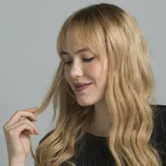 Mujer rubia con ondas, tocando su cabello. Aprende como matizar el pelo con tinte en casa para un look radiante.