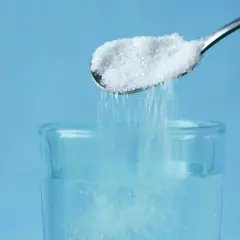 Cuchara con sal cayendo en un vaso de agua, un método para aclarar el pelo de forma natural.