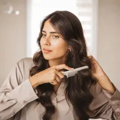 Mujer peinando su cabello oscuro y ondulado, mostrando una envidiable densidad capilar.