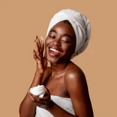 Mujer sonriente con toalla en la cabeza aplica crema con niacinamida y ácido salicílico.