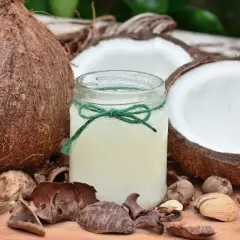 Aceite de coco para que sirve: un frasco de aceite de coco rodeado de cocos enteros y partidos, ideal para la piel y el cabello.
