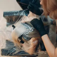 Manos enguantadas aplican tinte al cabello rubio. Es tiempo de tinte pelo para un cambio de look.