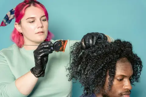 Mujer con pelo rosa aplica tinte a cabello rizado. ¿Cuánto dura un tinte de pelo? Depende del cuidado.