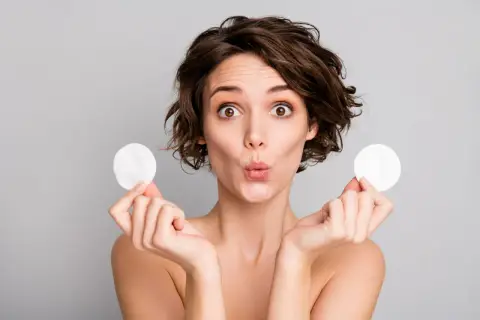 Mujer sorprendida con discos de algodón, mostrando para que sirve el agua micelar para una limpieza facial suave y efectiva.