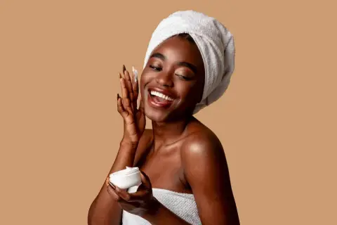 Mujer sonriente con toalla en la cabeza aplica crema con niacinamida y ácido salicílico.
