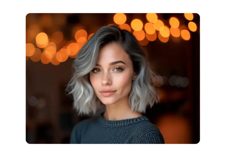 Mujer con pelo corto rubio platino ceniza, mirada cautivadora y luces cálidas de fondo.