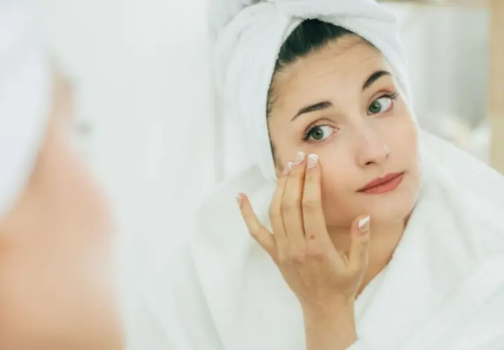 Mujer con toalla en la cabeza aplicándose crema, buscando productos que significan no comedogénico para cuidar su piel.