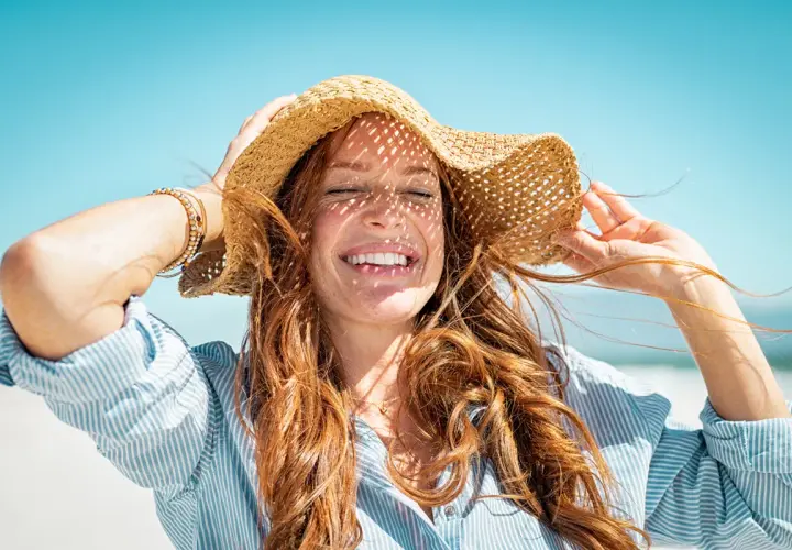 Mujer sonríe con sombrero de paja, aprendiendo como cuidar el pelo en verano.