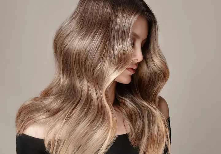 Mujer con cabello largo y ondulado, con un degradado de color que va de oscuro a rubio. Un ejemplo de cómo aclarar el pelo teñido para un look natural.