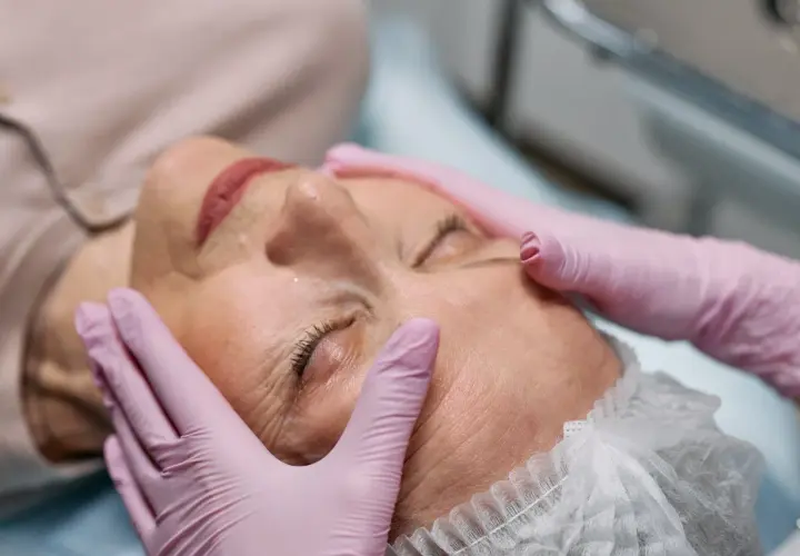 Manos enguantadas realizan tratamiento de radiofrecuencia en la cara de una mujer, buscando rejuvenecer su piel.