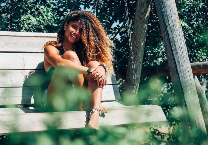 Chica con pelo rizado y voluminoso, sonriendo sentada en un columpio. ¡Así se consigue como rizar el pelo con espuma!