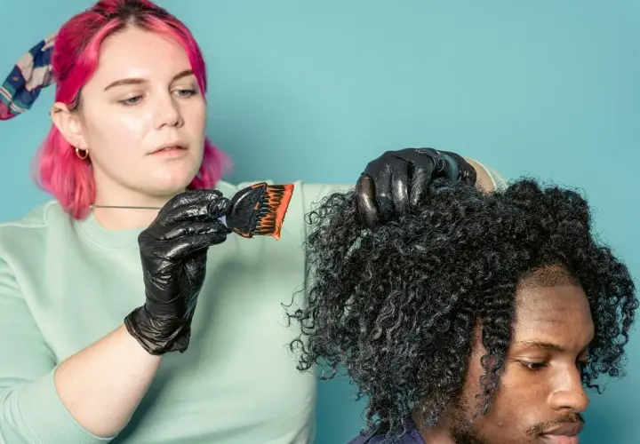 Mujer con pelo rosa aplica tinte a cabello rizado. ¿Cuánto dura un tinte de pelo? Depende del cuidado.
