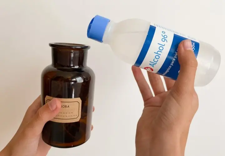 Manos vierten alcohol de romero en un frasco de vidrio ámbar. El alcohol de romero sirve para desinfectar y aliviar dolores.