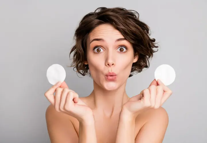 Mujer sorprendida con discos de algodón, mostrando para que sirve el agua micelar para una limpieza facial suave y efectiva.
