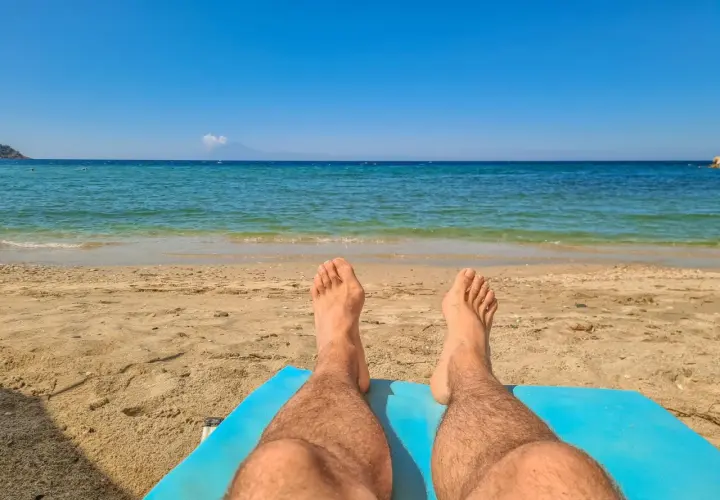 Piernas bronceándose en la playa. El sol de las 7 de la tarde pone moreno mientras disfrutas del mar azul y la arena dorada.