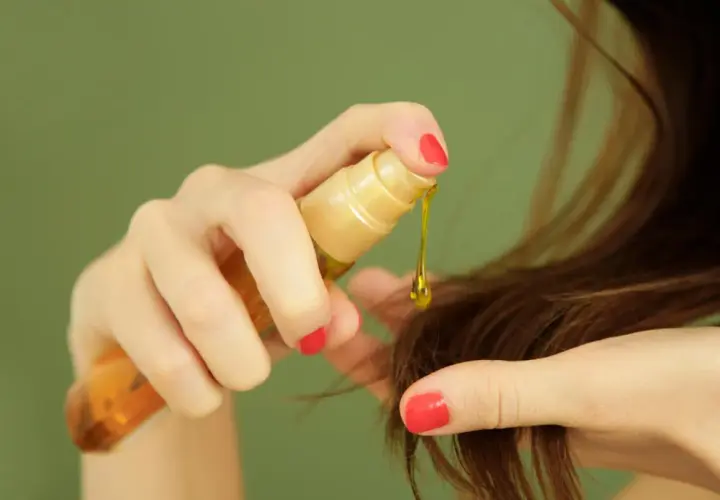 Manos aplicando aceite de ricino para el pelo, una gota dorada cae sobre las puntas.