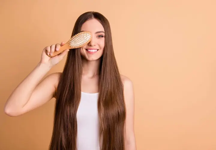 Mujer sonriente con pelo largo y liso, usando un cepillo de madera para mostrar cómo desenredar un pelo muy enredado.