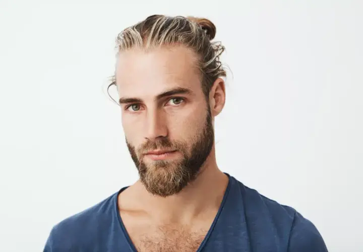 Chico con barba y mechas rubias recogidas en un moño. Su mirada es intensa y directa.