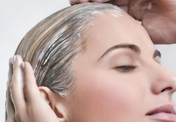 Manos aplican mascarilla en pelo seco antes de lavar, nutriendo cada hebra para un cabello suave y brillante.