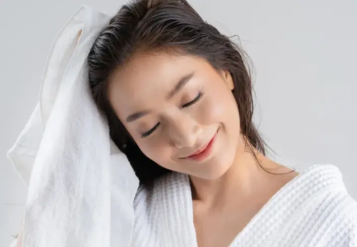 Mujer secándose el pelo con una toalla blanca. Recuerda, es malo dormir con el pelo mojado.