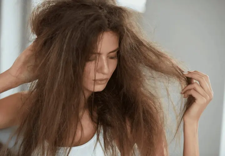 Mujer con pelo fosco y enredado, tocándose la cabeza con una mano y examinando un mechón con la otra.