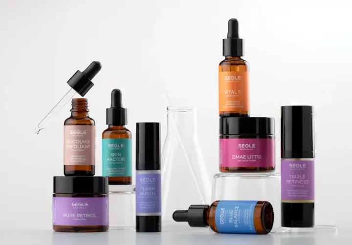 Varias botellas y tarros de productos de cuidado de la piel Segle, incluyendo el serum cuando se aplica, sobre un fondo blanco.
