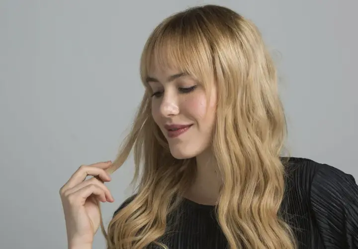 Mujer rubia con ondas, tocando su cabello. Aprende como matizar el pelo con tinte en casa para un look radiante.