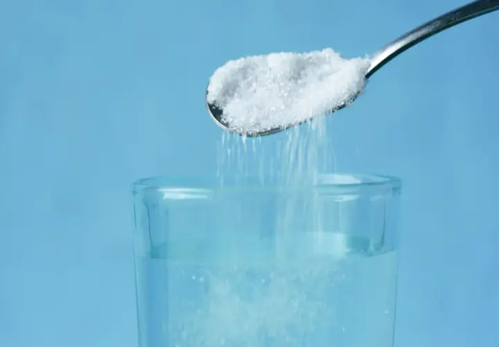 Cuchara con sal cayendo en un vaso de agua, un método para aclarar el pelo de forma natural.