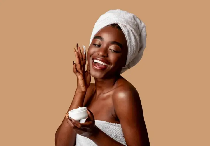 Mujer sonriente con toalla en la cabeza aplica crema con niacinamida y ácido salicílico.