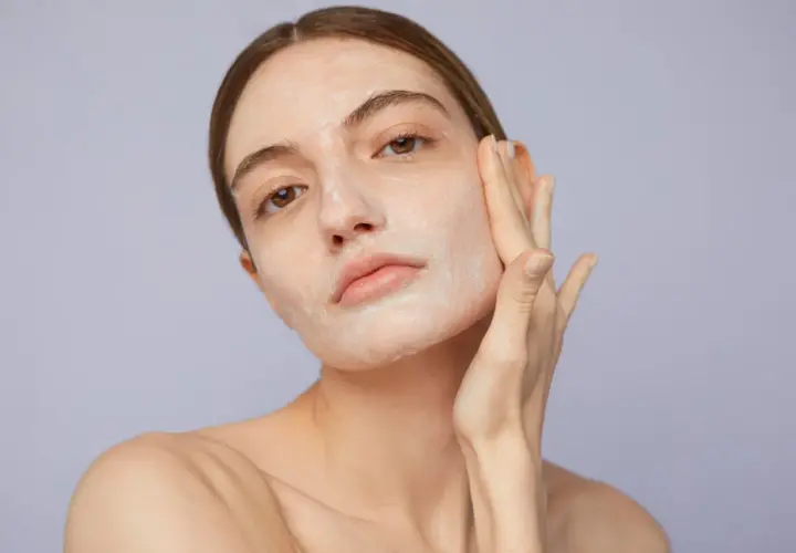 Mujer aplicándose crema en el rostro, un paso clave para saber como exfoliar la piel y lograr un cutis radiante.