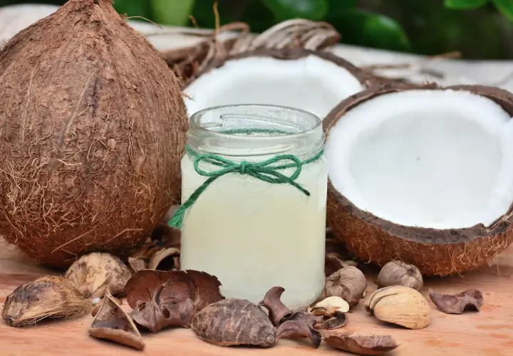 Aceite de coco para que sirve: un frasco de aceite de coco rodeado de cocos enteros y partidos, ideal para la piel y el cabello.