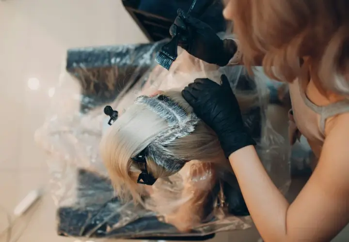 Manos enguantadas aplican tinte al cabello rubio. Es tiempo de tinte pelo para un cambio de look.