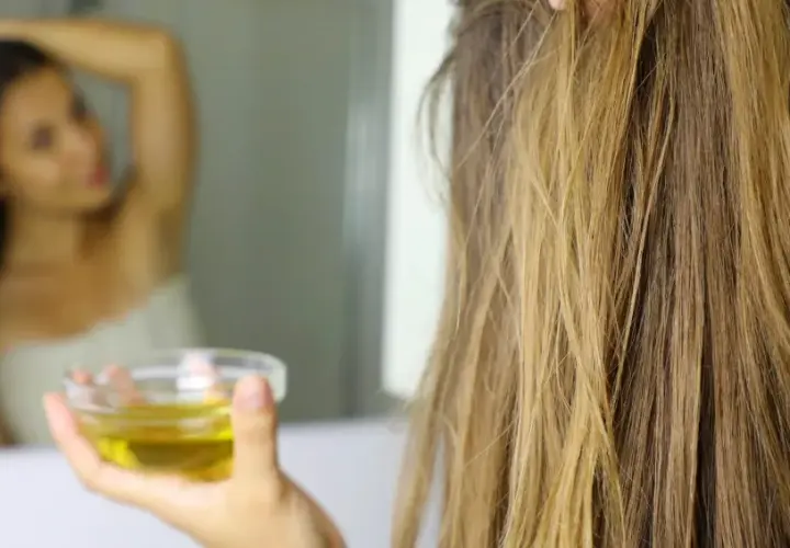 Mujer se aplica aceite de oliva en el pelo, demostrando que el aceite de oliva es bueno para el pelo.