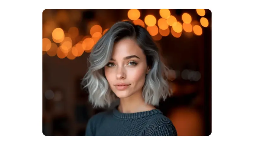 Mujer con pelo corto rubio platino ceniza, mirada cautivadora y luces cálidas de fondo.